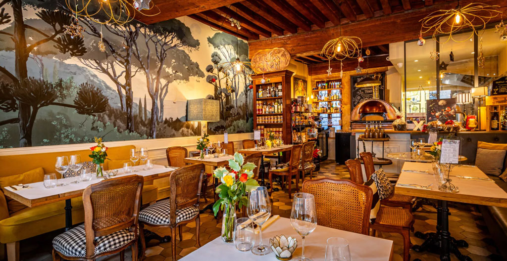 Intérieur chaleureux de pizzeria artisanale familiale avec tables en bois dressées et four à bois traditionnel en brique visible en arrière-plan